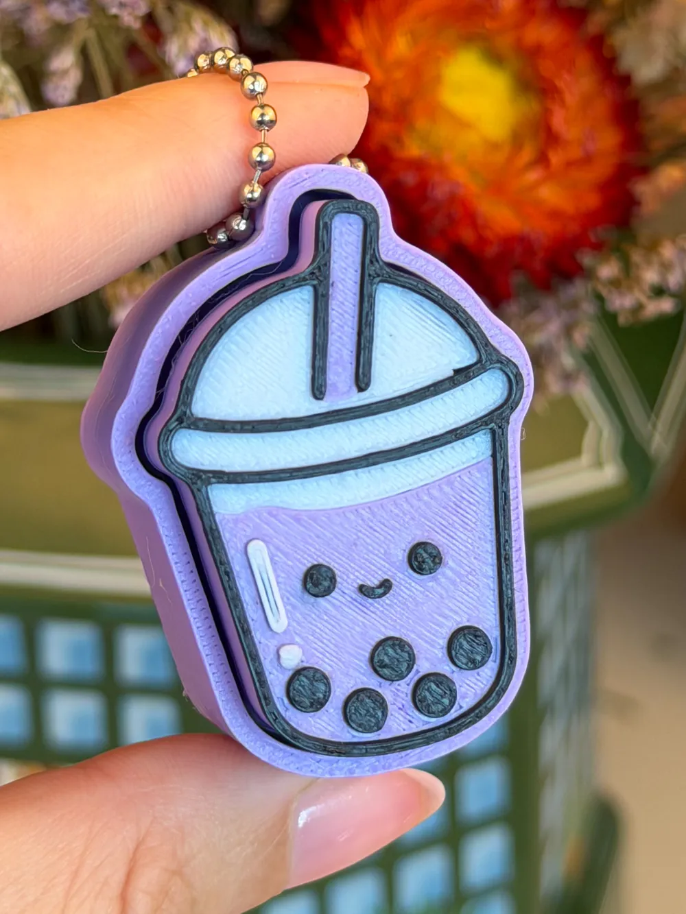 A lilac bubble-tea clicker with a smiling face and tapioca pearls, held between finger and thumb