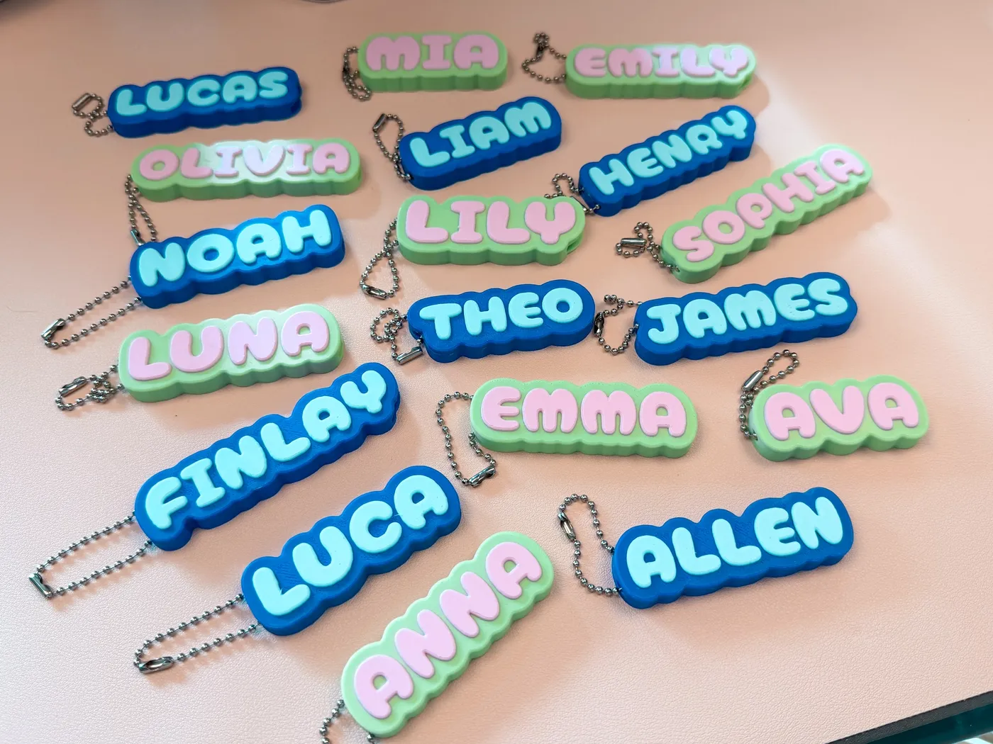 Eighteen printed name can openers laid out on a desk, each a different name in pink or blue